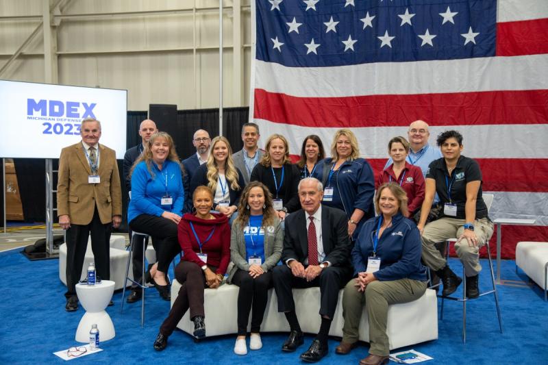 A group of people sitting in front of a large American flag.