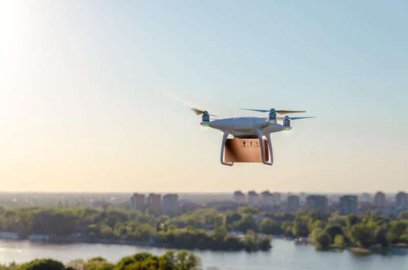 Drone carrying delivering package, city in background.
