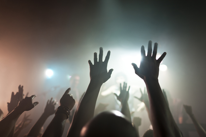 a crowd at a live music venue pointing and reaching up towards the performers