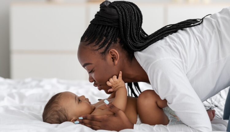 Black mom playing in bed with her infant, kissing baby