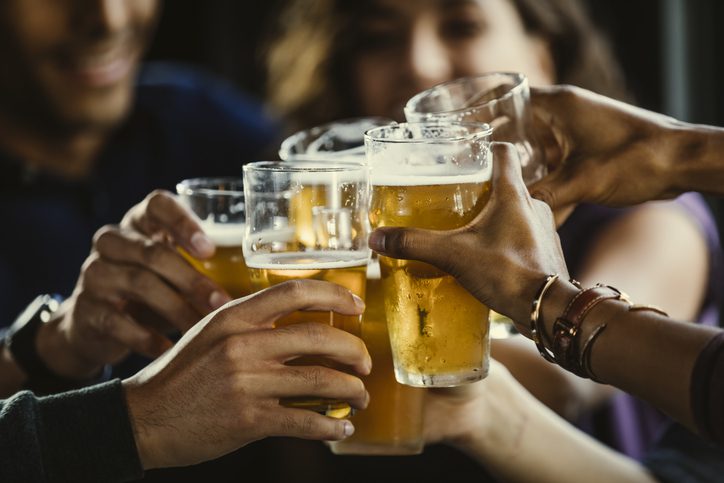 Group of friends toasting beer glasses at table in bar