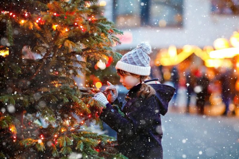 Little cute kid girl having fun on traditional Christmas market during strong snowfall.