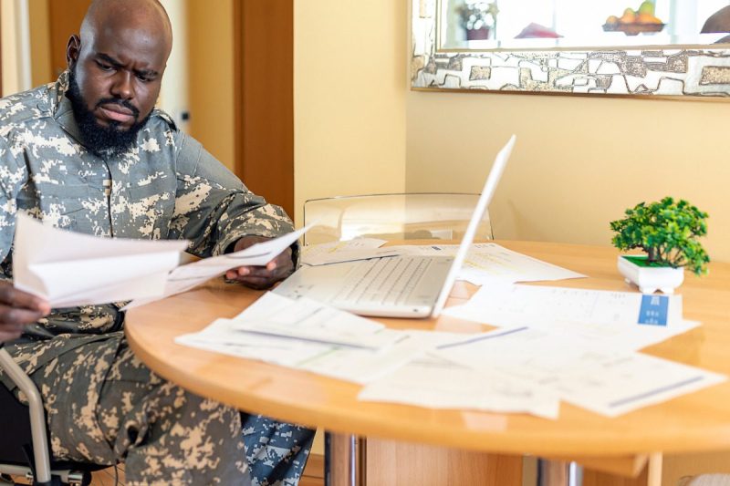 Disabled Veteran US Marine Soldier in Wheelchair. Worried African Veteran in Wheelchair is Looking at Financial Bills at the Home