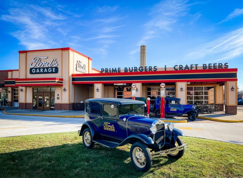 a vintage blue car in front of a restaurant advertising burgers and beers